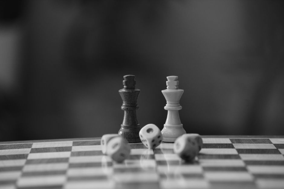 Black and white photo depicting chess pieces and dice on a chessboard, highlighting strategy and chance.