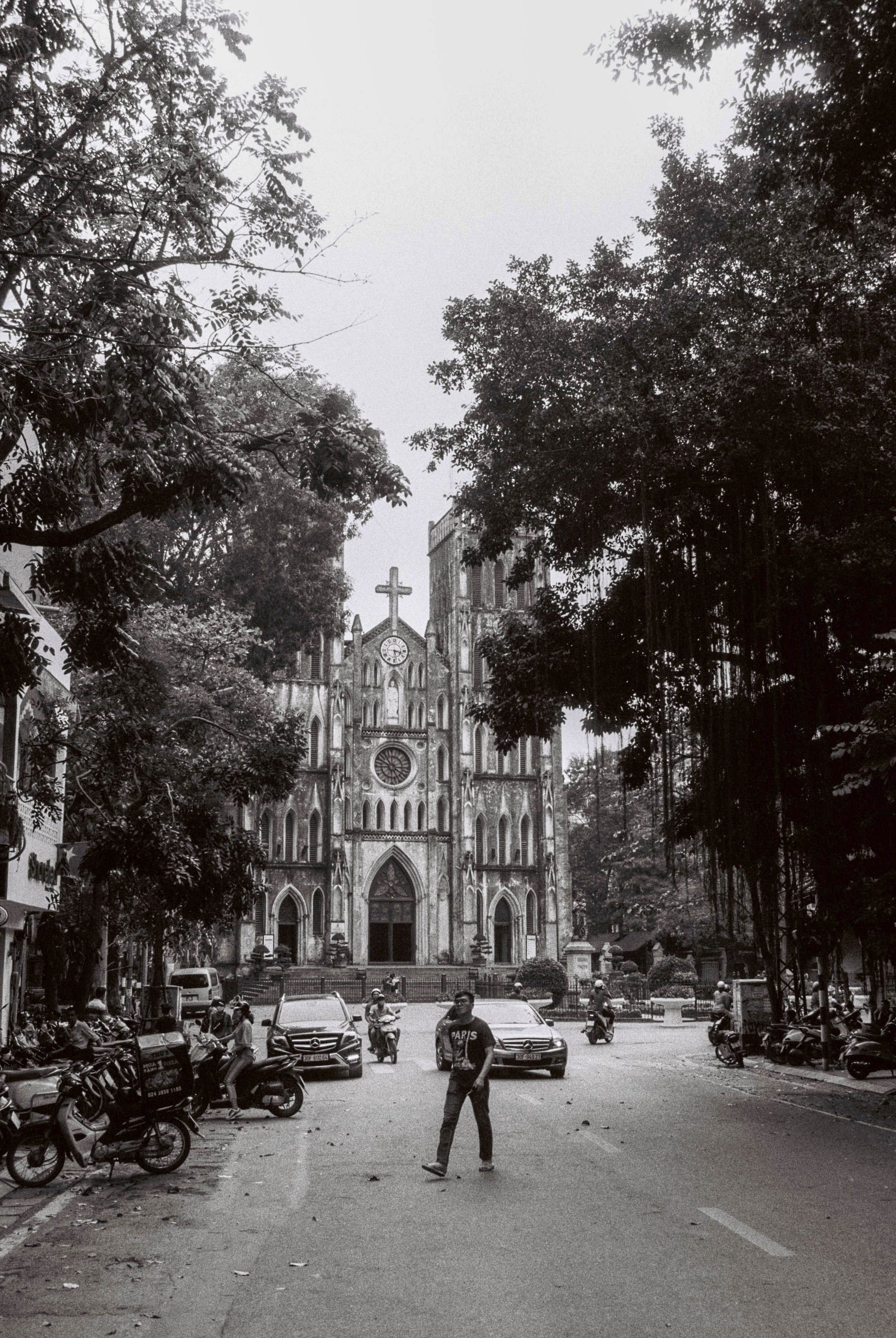 Black and white street view of St. Joseph's Cathedral in Hanoi, Vietnam with motorbikes.