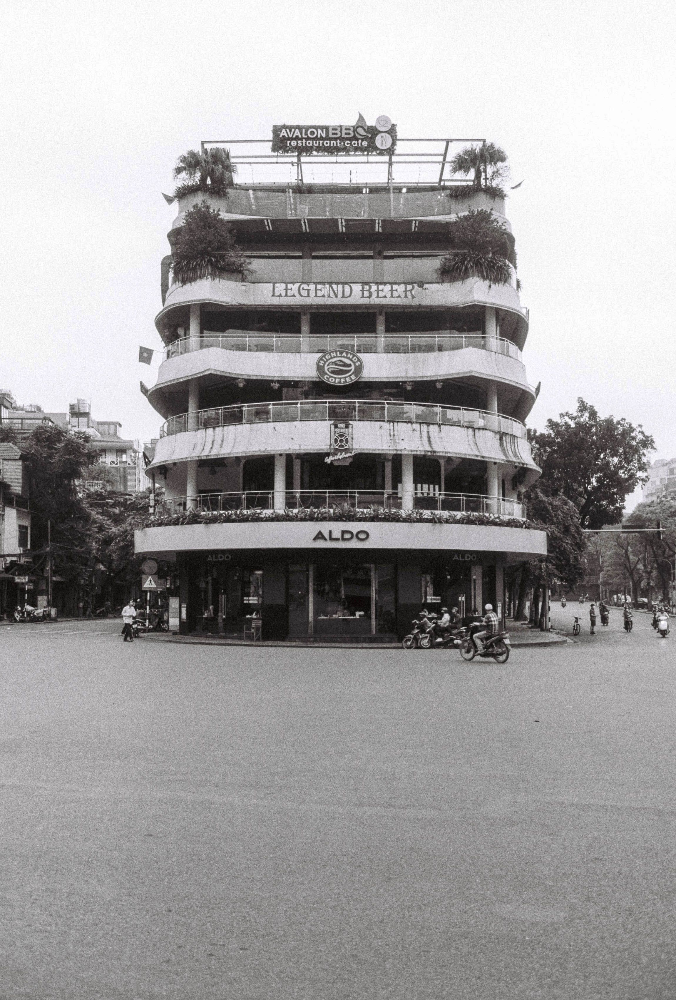 Black and white photo of a multi-level building in Hanoi, capturing urban architecture and street life.