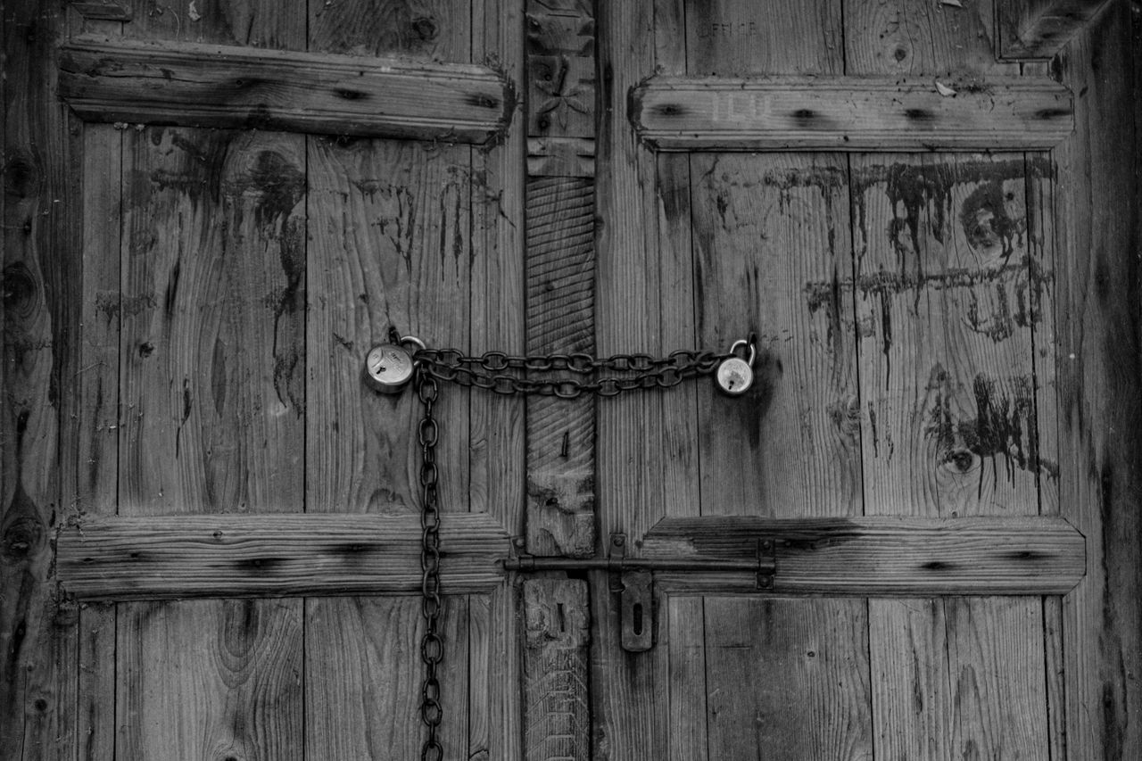 a black and white photo of a rustic wooden door secured with a chain a