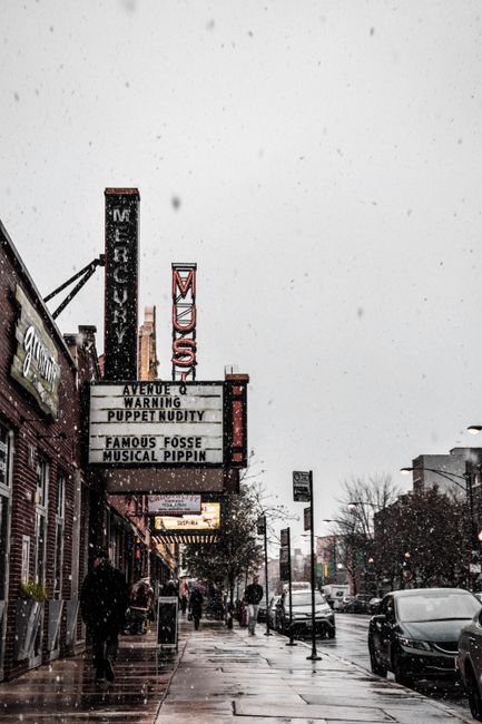 A bustling urban street in winter with theater signs, snowfall, and people walking.