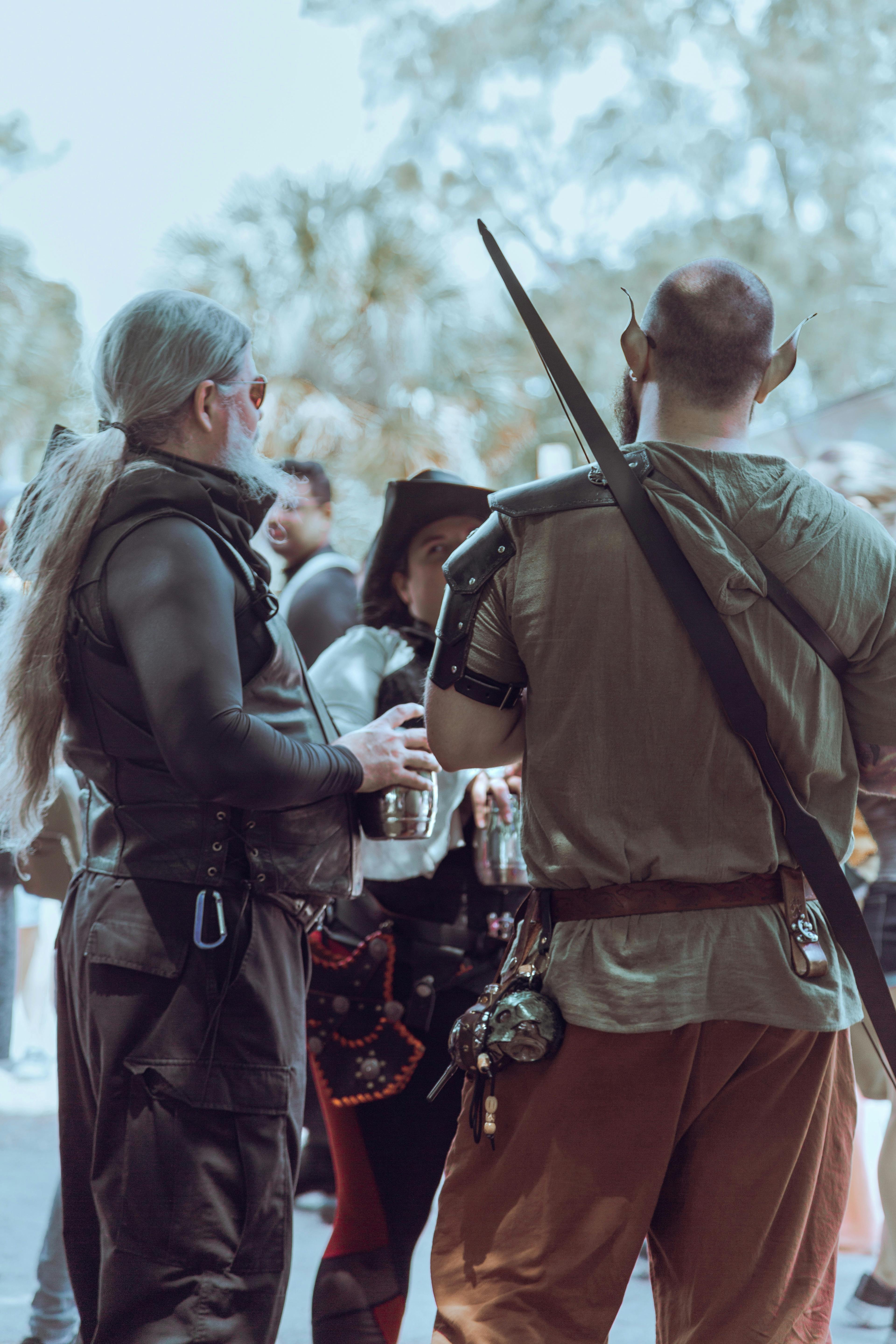 Adults in fantasy costumes gather outdoors, immersed in a lively festival setting.