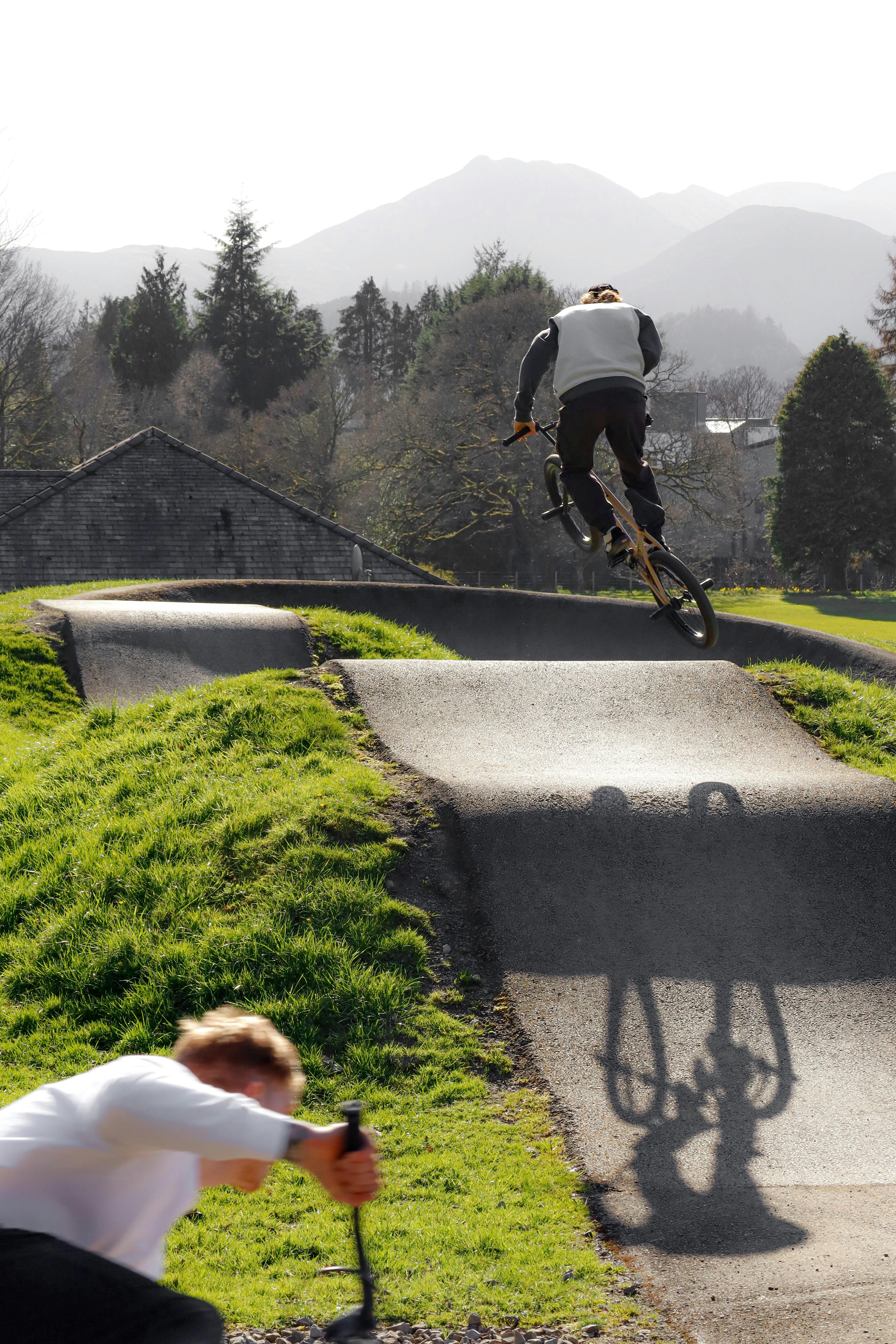 BMX rider performing a midair trick in a green, outdoor skatepark with mountains in the background.
