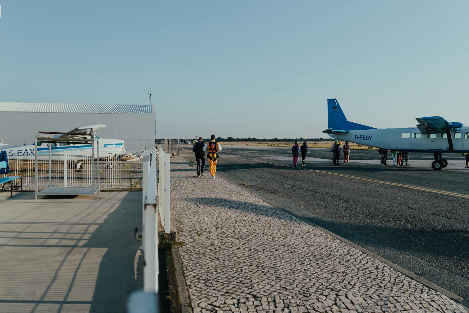 Skydivers preparing to board a small airplane on a sunny day at the airport runway.