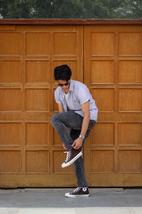 Free Stylish young man adjusts his sneaker while standing against a wooden wall outdoors. Stock Photo