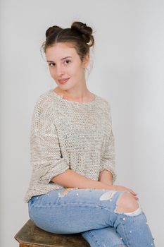 Casual portrait of a young woman in a sweater sitting on a stool indoors.