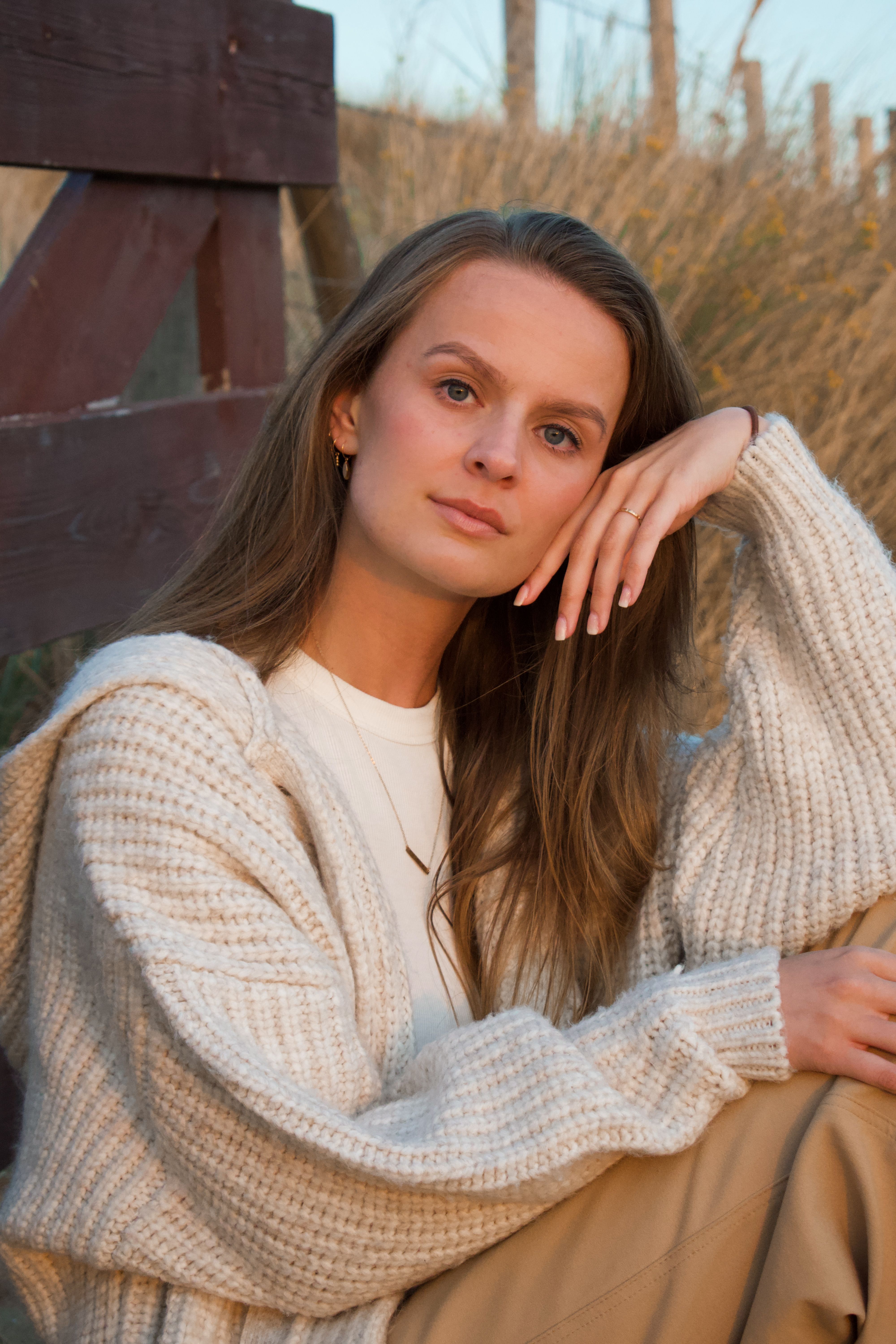 Portrait of a woman sitting outdoors in a knit sweater, exuding warmth and tranquility.