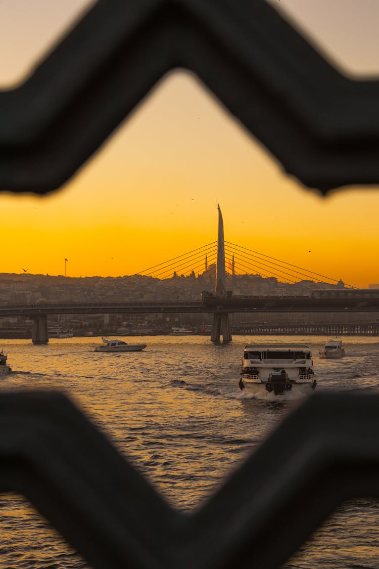 Ferry Sailing Near Halic Bridge Behind Gap In Railing Gaps At Sunset