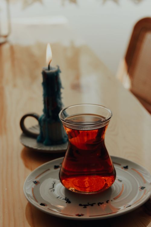 Free A glass of tea and a lit blue candle create a warm, cozy atmosphere on a wooden table. Stock Photo