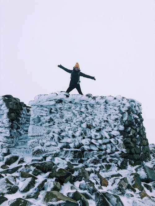 Woman Standing on Top of a Snowy Rock Formation with Her Arms Spread 