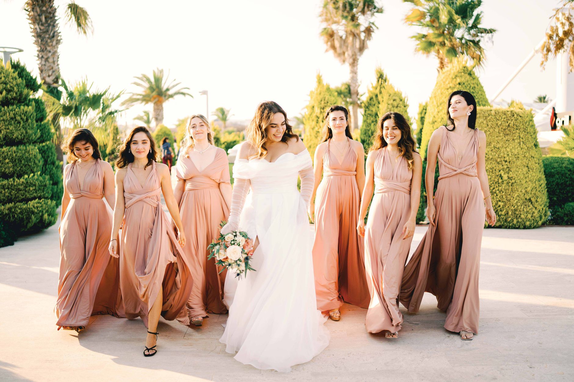 Bride and bridesmaids walking together happily in sunlight outdoors.