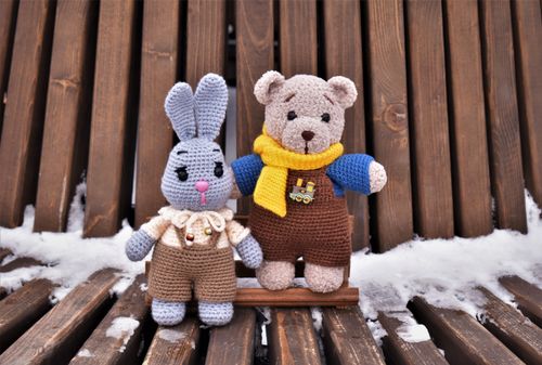 Free Handmade crochet bunny and teddy bear toys seated on a snowy wooden bench, showcasing warmth and creativity. Stock Photo