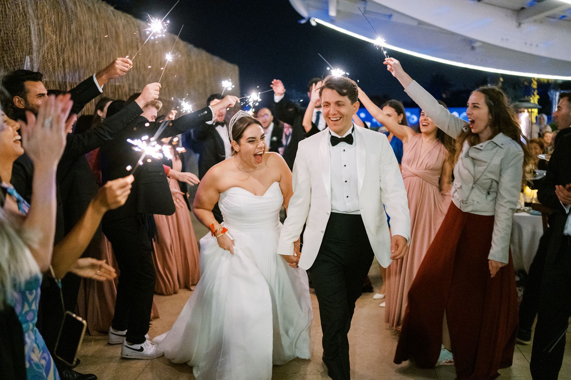 luxury wedding entertainment Egypt — Bride and groom celebrating among guests with sparklers during an evening wedding party.