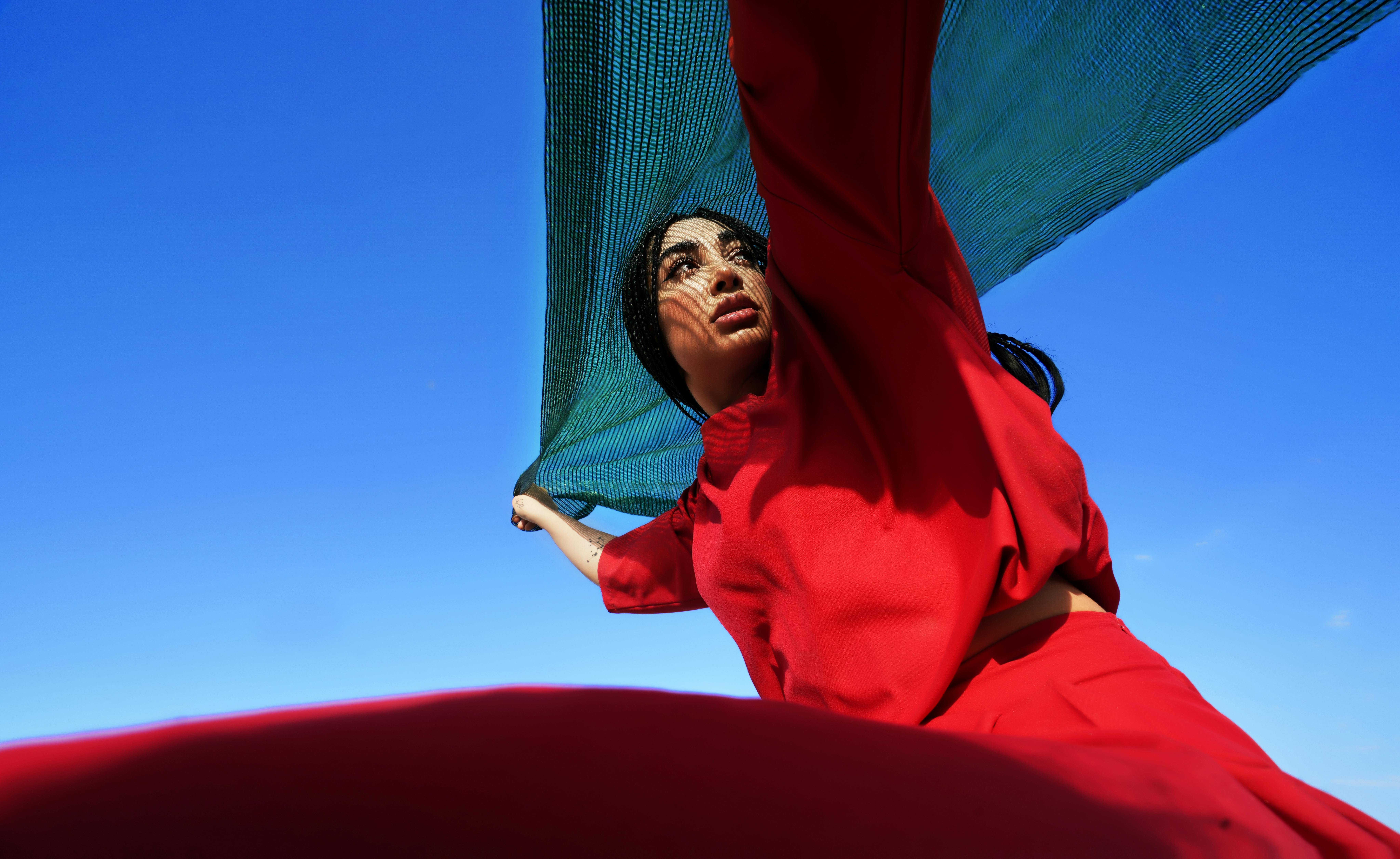 Striking image of a woman in red clothing holding a green scarf against a vibrant blue sky.