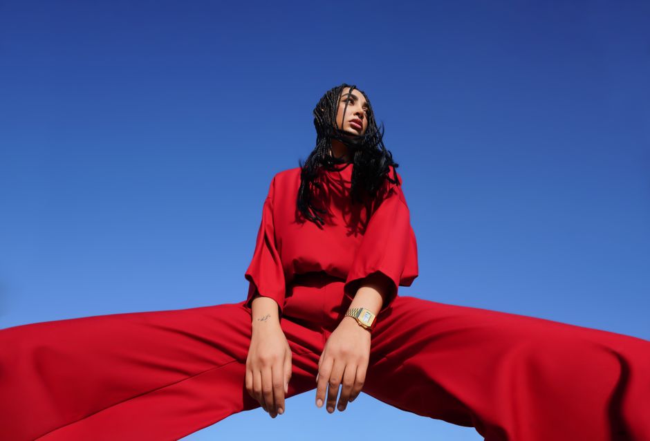 Dynamic fashion photo featuring a model in a vibrant red outfit against a clear blue sky.