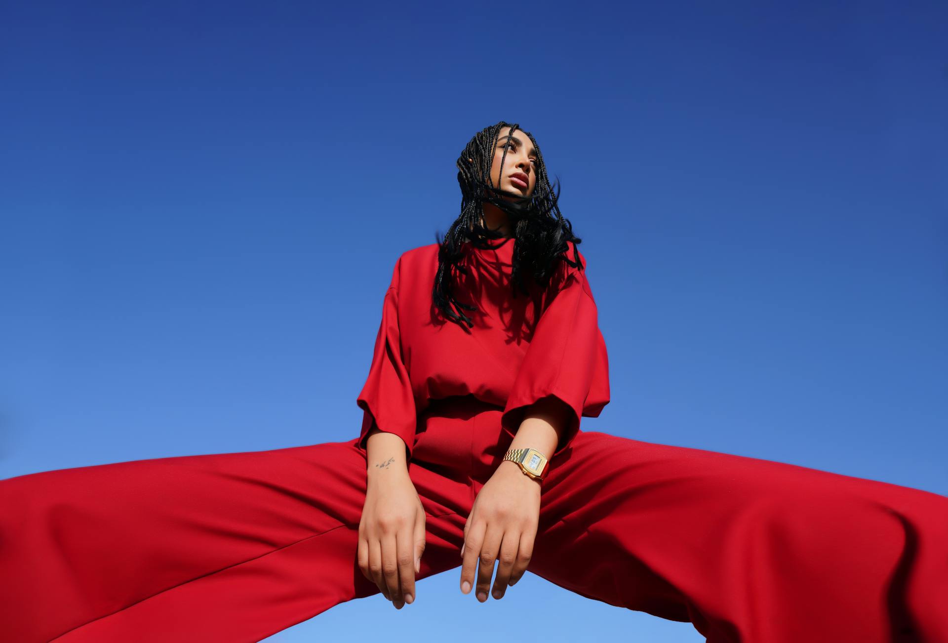 Dynamic fashion photo featuring a model in a vibrant red outfit against a clear blue sky.