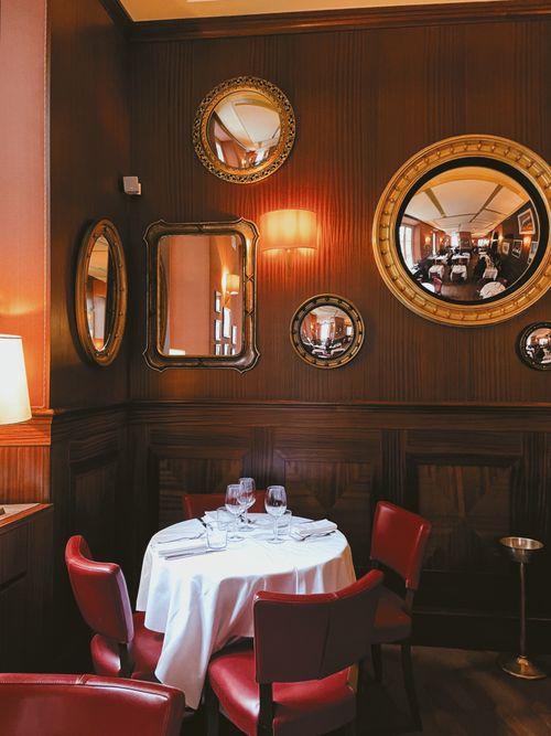 Free Cozy restaurant scene featuring elegant mirrors and a set dining table against wood-panelled walls. Stock Photo