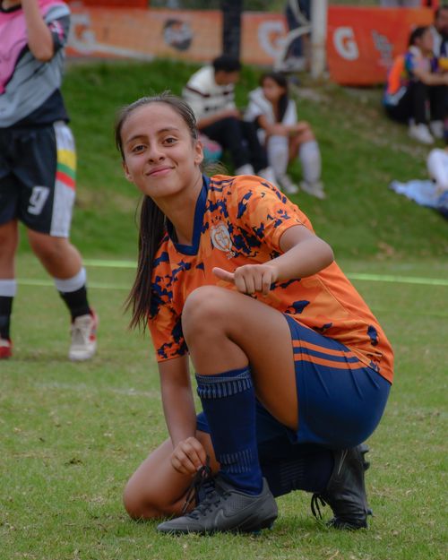 Free A young female soccer player crouches on the field, smiling and posing during a match. Stock Photo