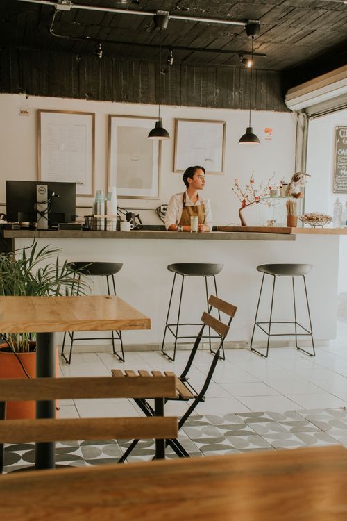 Free Warm café interior featuring a barista behind the counter, ideal for coffee lovers and modern spaces. Stock Photo