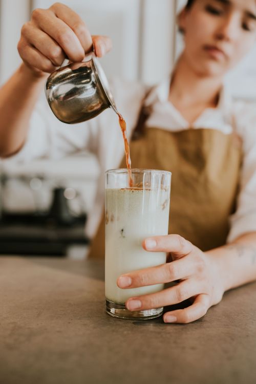 Free A barista carefully pours espresso into a glass of iced milk at a café. Stock Photo