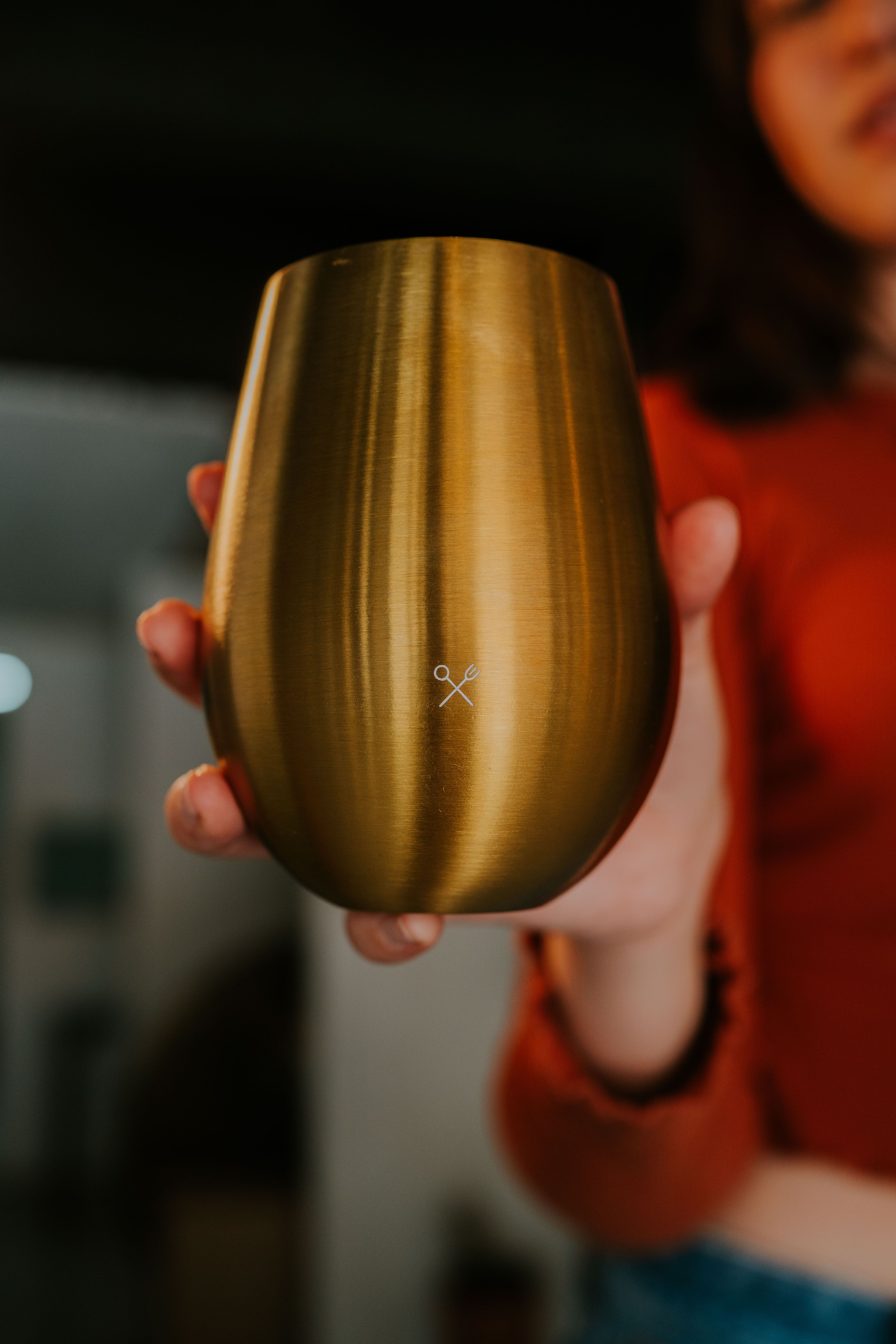 Stylish gold cup held by woman, modern indoor setting, warm ambiance.