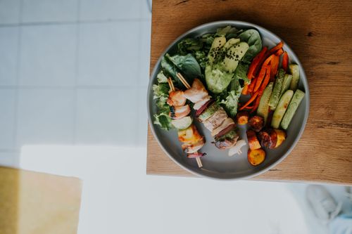 Free Top view of a vibrant platter with grilled skewers and fresh vegetables on a wooden table. Stock Photo
