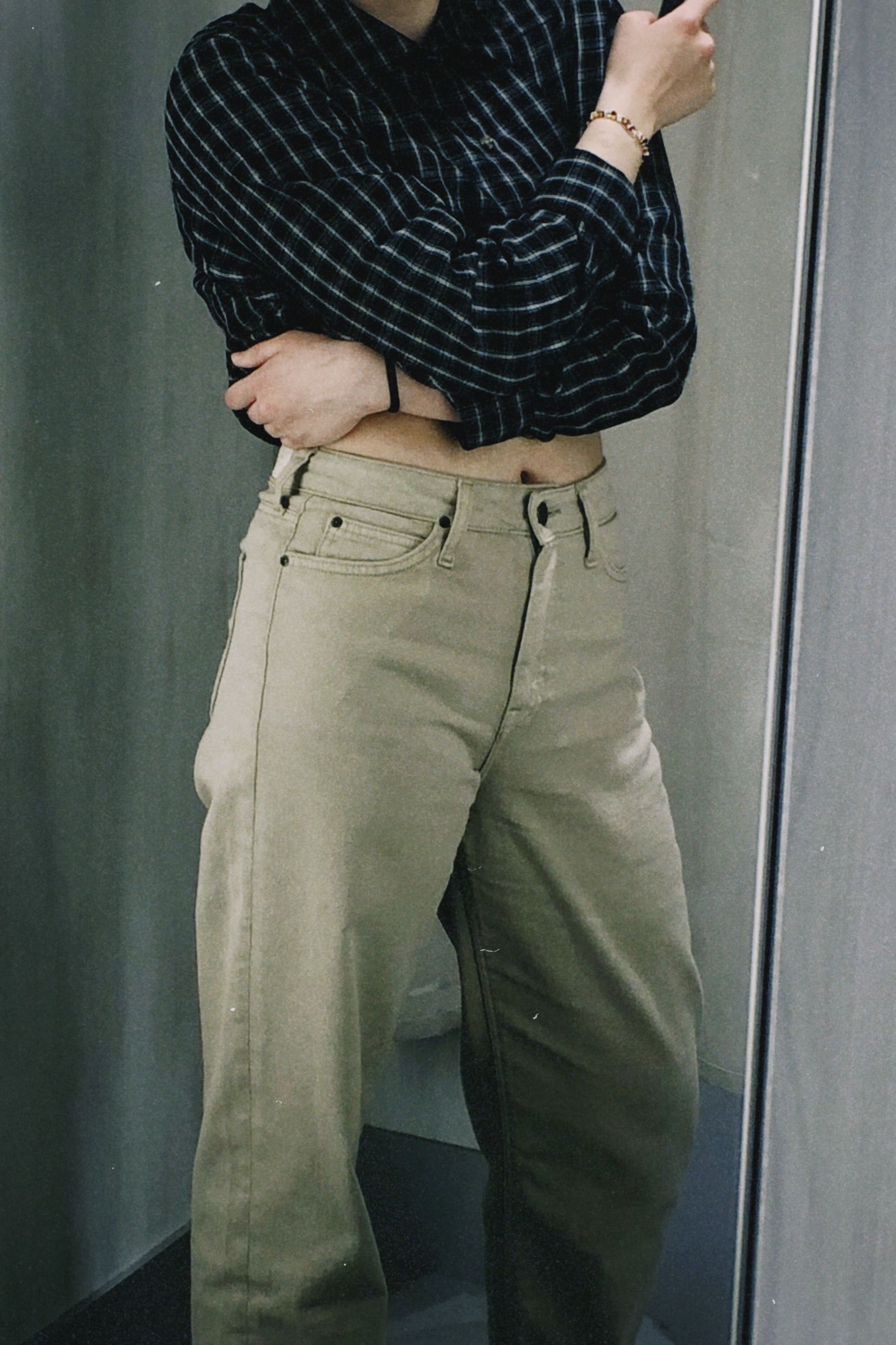 Woman in a crop top and pants posing in a mirror, showcasing casual fashion style.