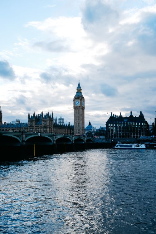 Free A scenic view of the Big Ben and Westminster Bridge against a dramatic evening sky from the River Thames. Stock Photo