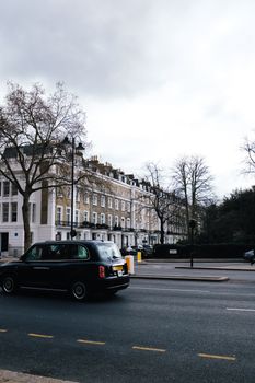 A quintessential London street scene featuring a black taxi cab, classic buildings, and overcast skies.