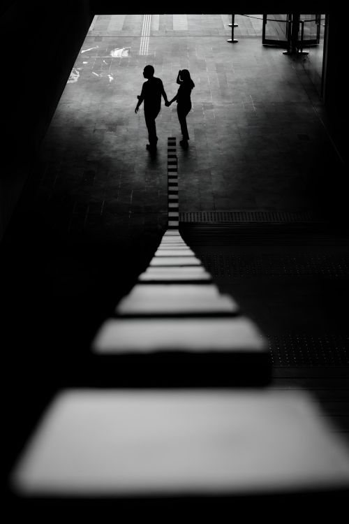 Free Black and white photo of a silhouetted couple holding hands, capturing a moment of connection in an urban setting. Stock Photo