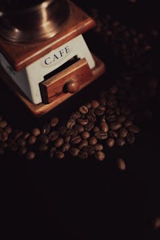 Close-up of a vintage coffee grinder surrounded by scattered coffee beans, capturing a rustic café vibe.