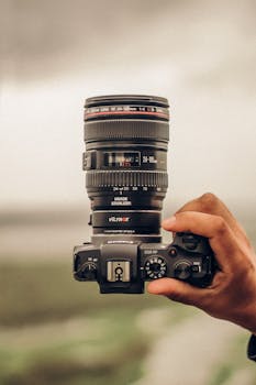 Close-up of a hand holding a DSLR camera in an outdoor setting.