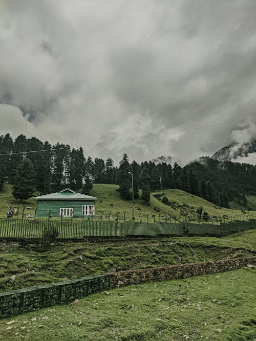 A Cabin on a Green Field under a Cloudy Sky 