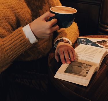 Warm scene with a person drinking coffee while reading a book indoors.