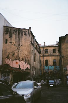 一条喜怒无常的城市小巷里，老建筑上涂着鸦，停着汽车