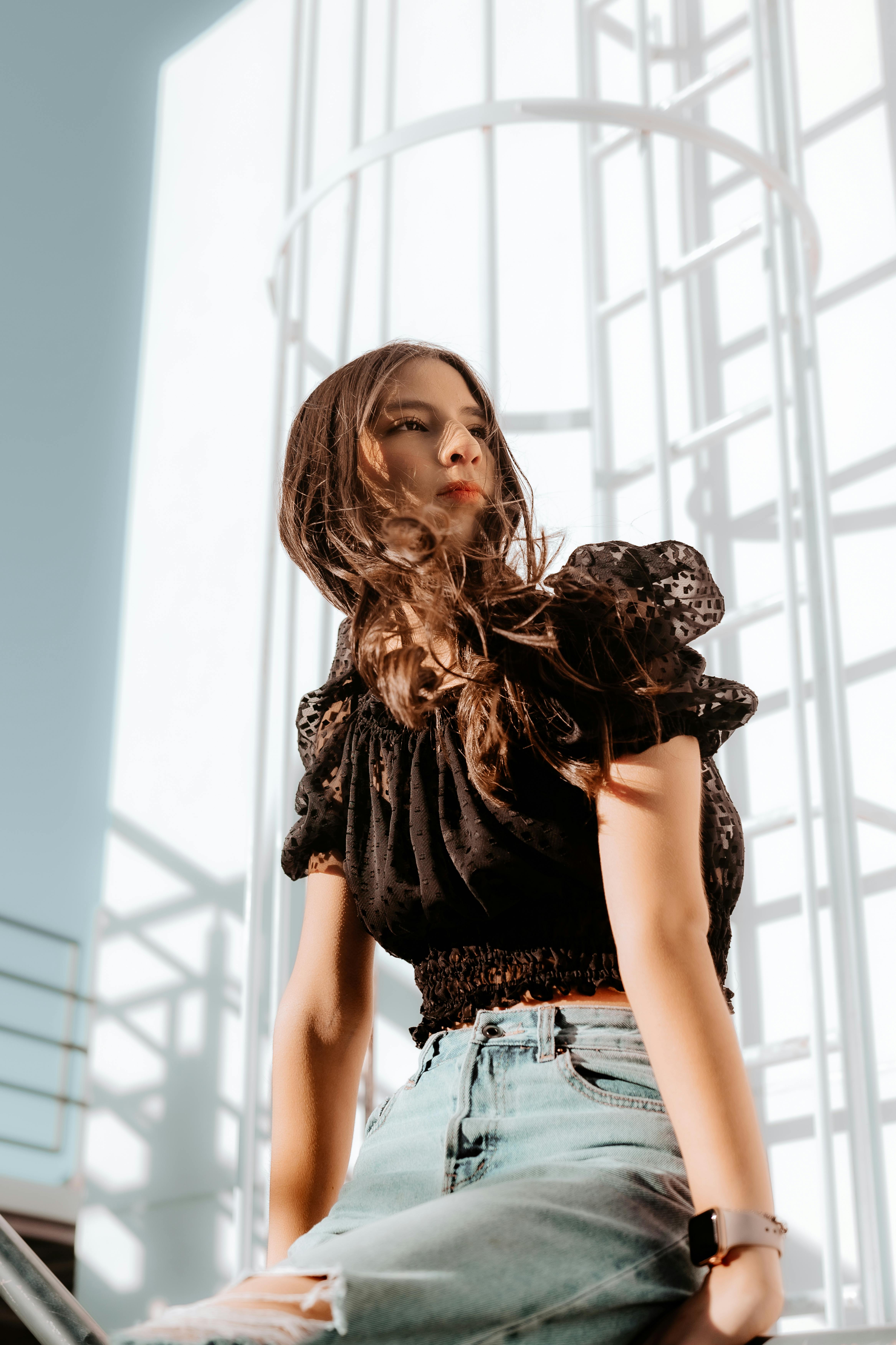 a woman in jeans and a black top sitting on a ledge