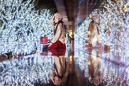 Young Woman Sitting in front of Illuminated with Christmas Lights Trees in City 