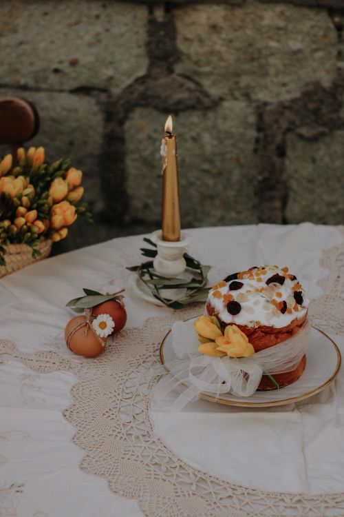 Free Easter cake with frosting and a lit candle on a rustic lace-covered table. Stock Photo