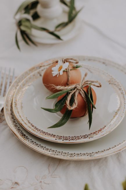 A rustic table setup featuring decorated eggs and a daisy on fine china plates for Easter.