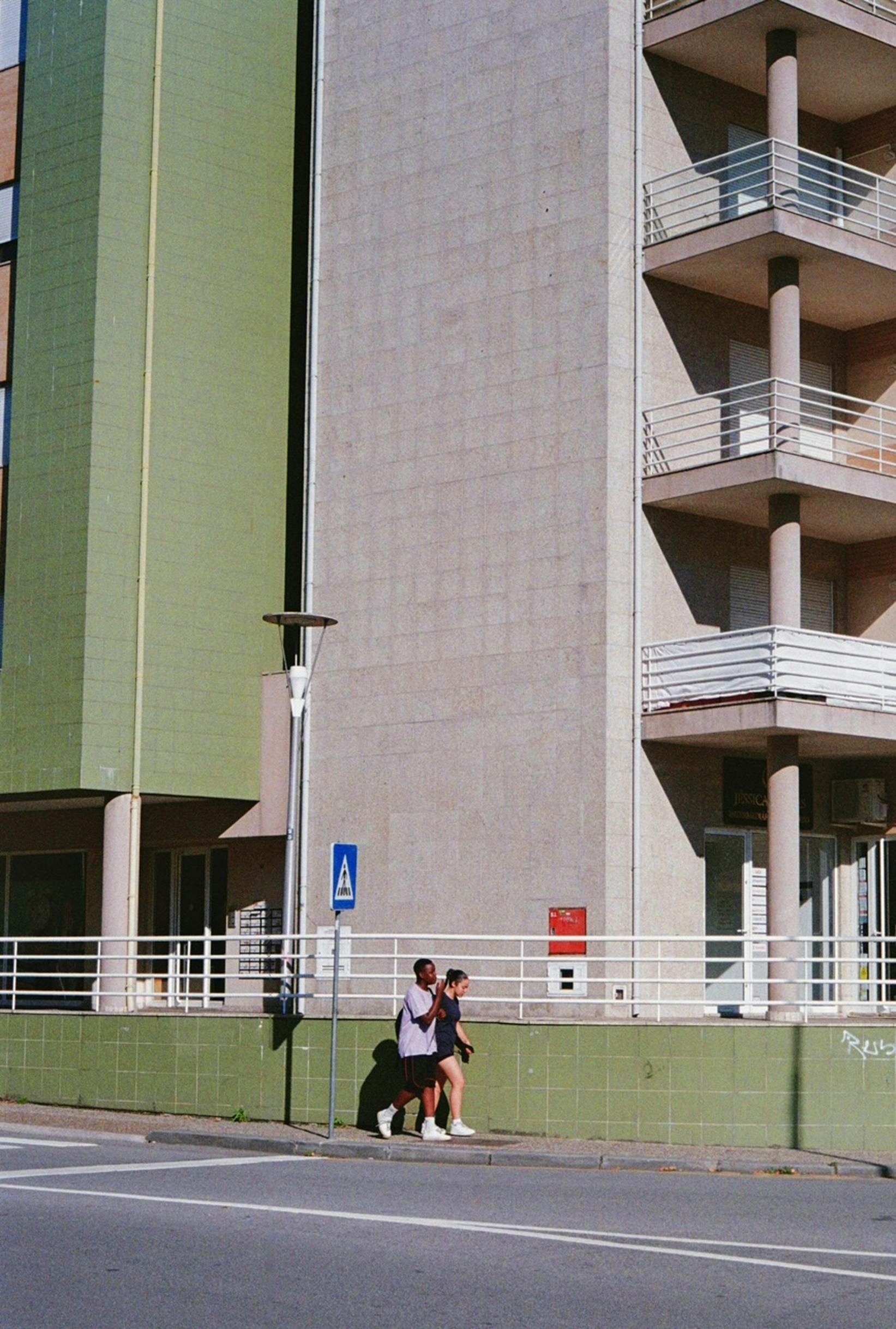 A couple walking past a modern apartment building on a sunny day.