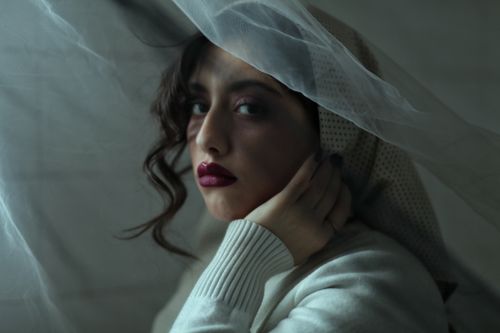 Free A dramatic portrait of a woman wearing a headscarf and veil, featuring striking red lips and a soft sweater. Stock Photo
