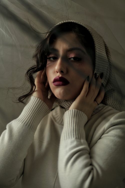 Free Elegant portrait of a woman with dark hair and scarf, showcasing dramatic makeup in soft lighting. Stock Photo