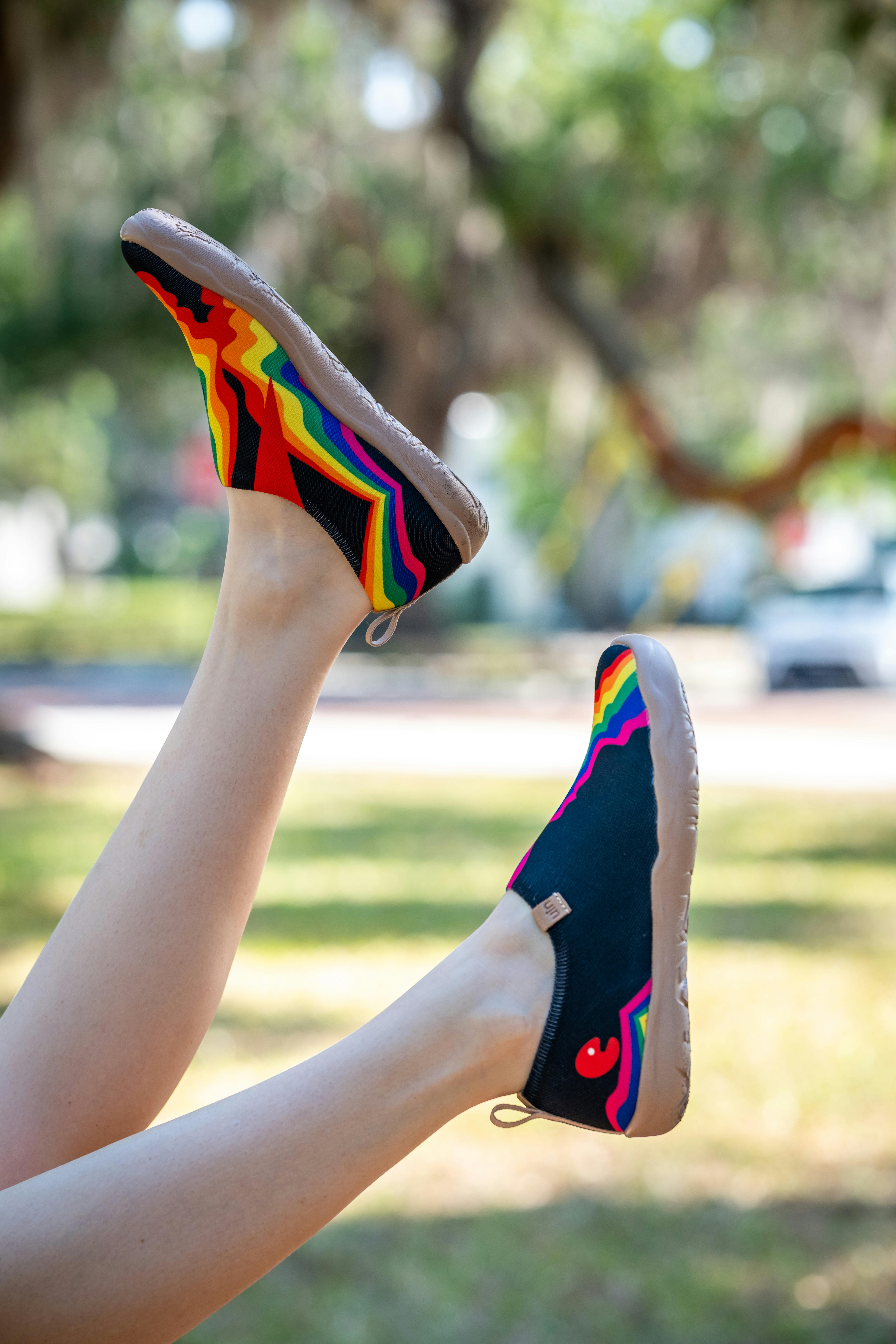 A pair of stylish shoes with vibrant rainbow patterns worn outdoors on a sunny day.