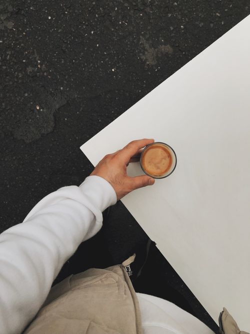 Free A hand holds a cup of espresso on a white table outdoors, seen from above. Stock Photo