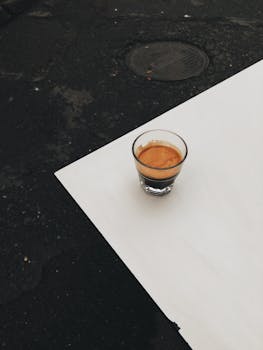 A single espresso shot in a glass on a stark white surface, showcasing simplicity.