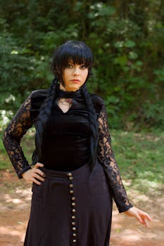 Young woman in gothic lace outfit with braids posing in a forest, showcasing a witchy, mysterious style.