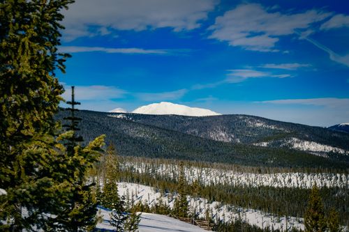 Free Breathtaking winter landscape with snow-covered mountains, evergreen trees, and blue sky. Stock Photo