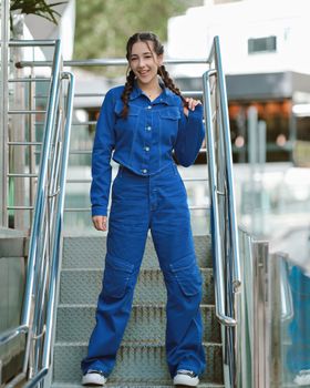 Smiling woman in blue denim outfit posing stylishly on stairs outdoors.