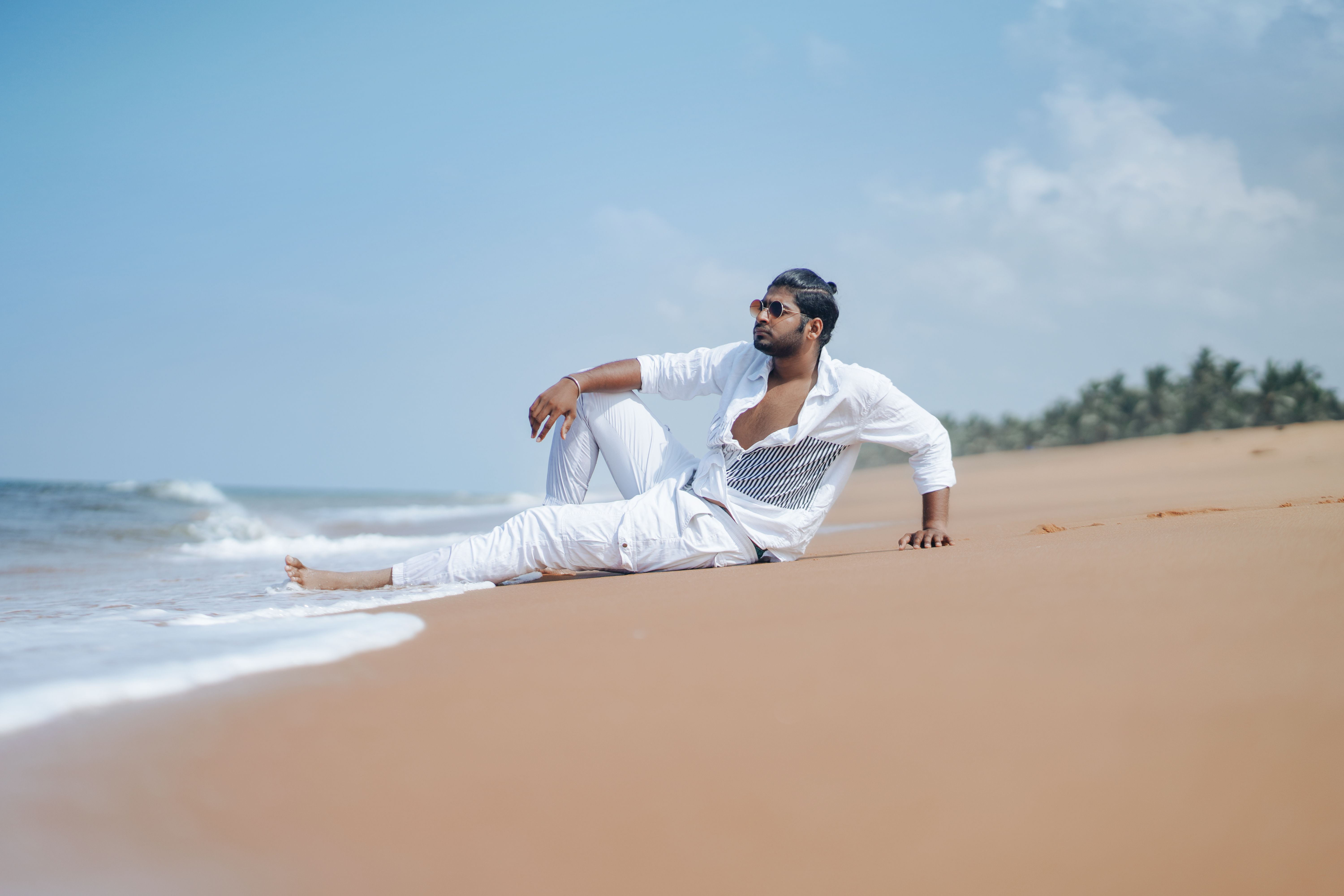 A man in a white outfit relaxes on a serene sandy beach, enjoying a sunny day.