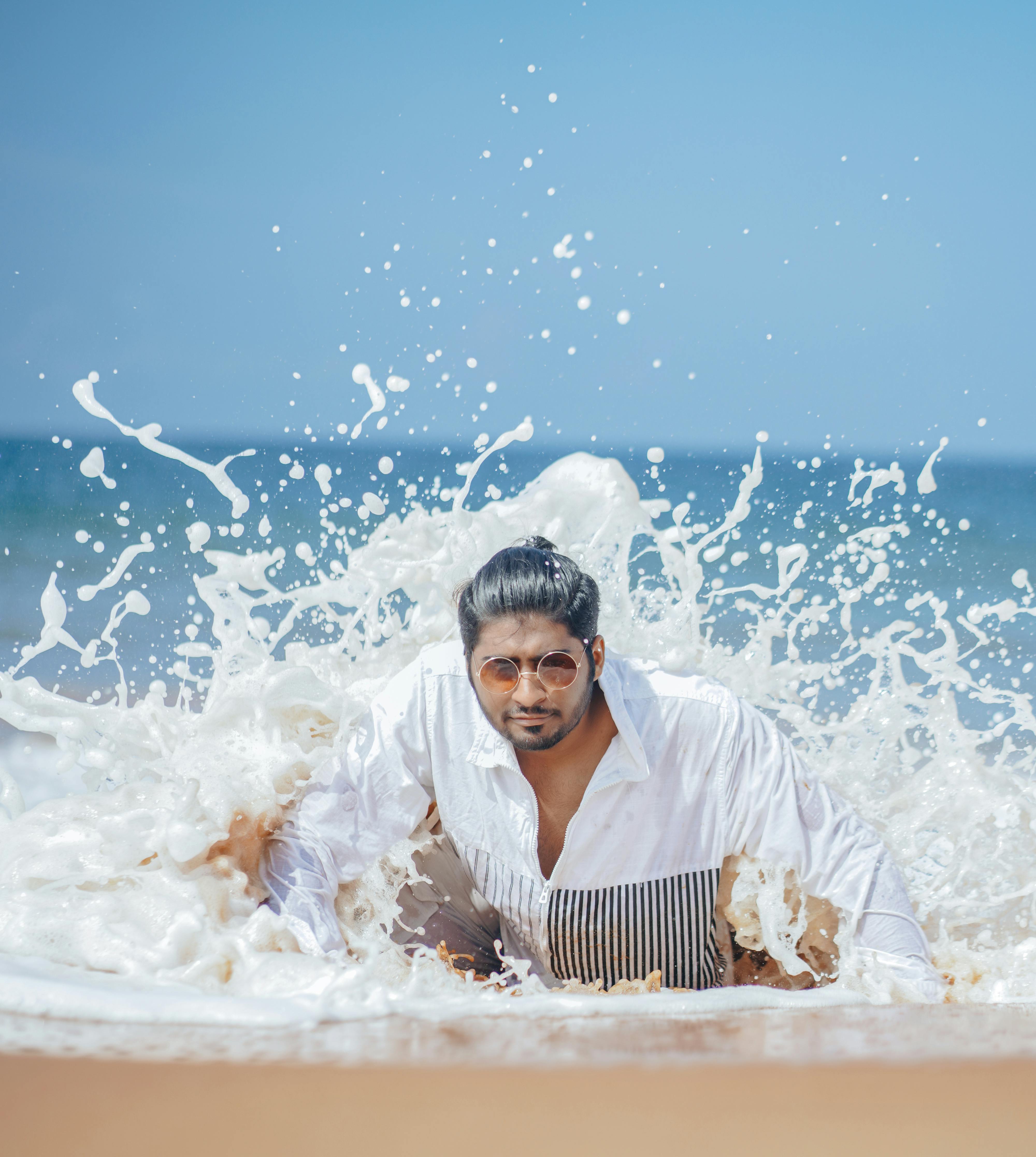 Stylish young man in a white shirt embracing ocean waves at the beach.